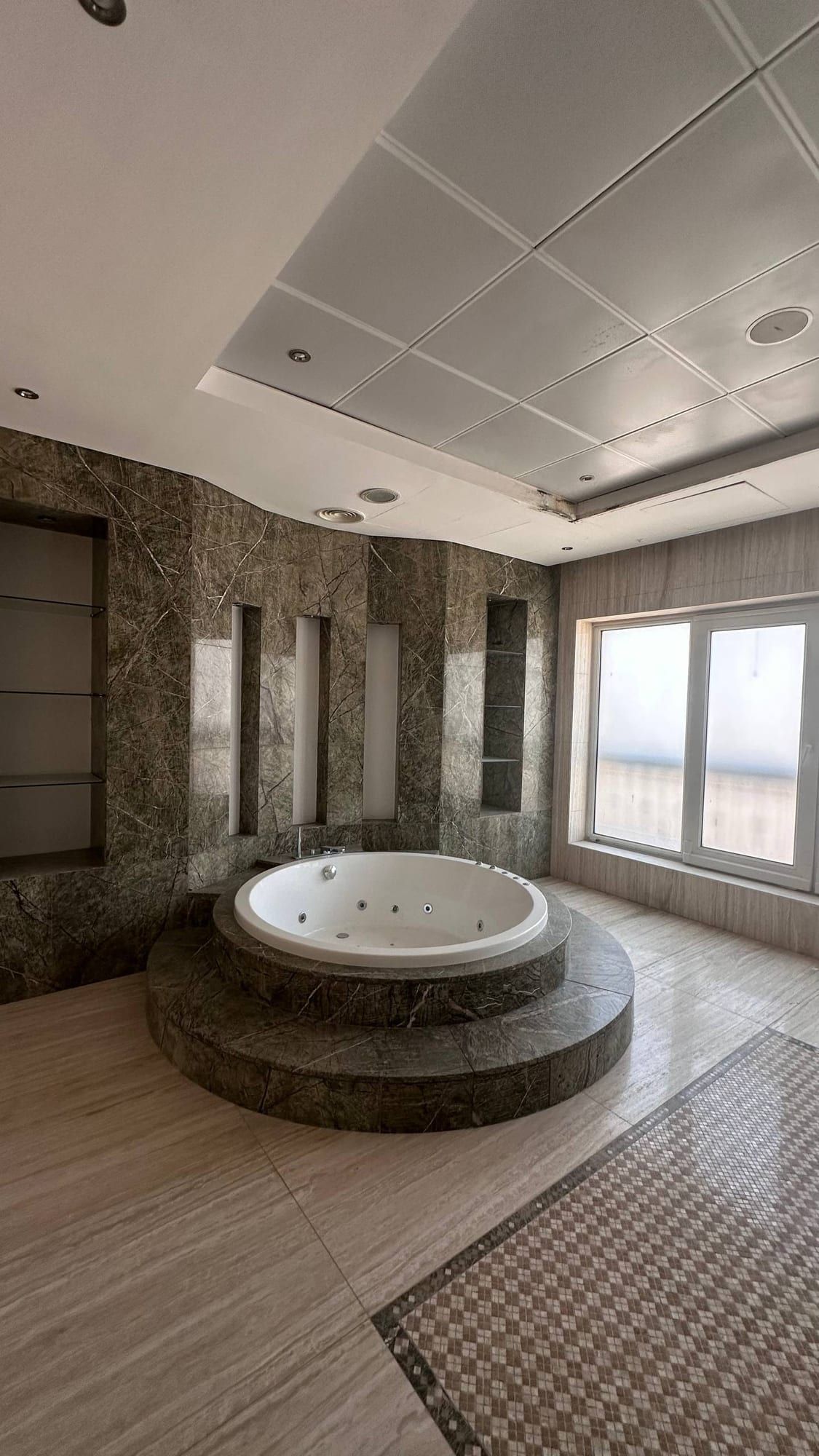 Bathroom with a raised round tub clad in stone and a tiled floor