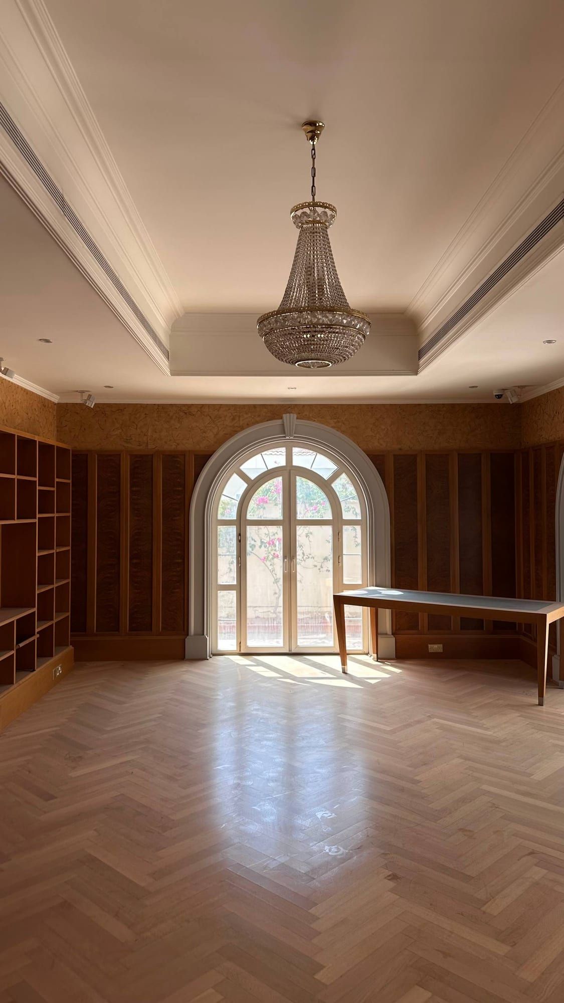 Library with timber shelving, a crystal chandelier and a tall arched window