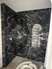 Bathroom wall clad floor to ceiling in dark stone with white veining, curved moulding pieces on the floor