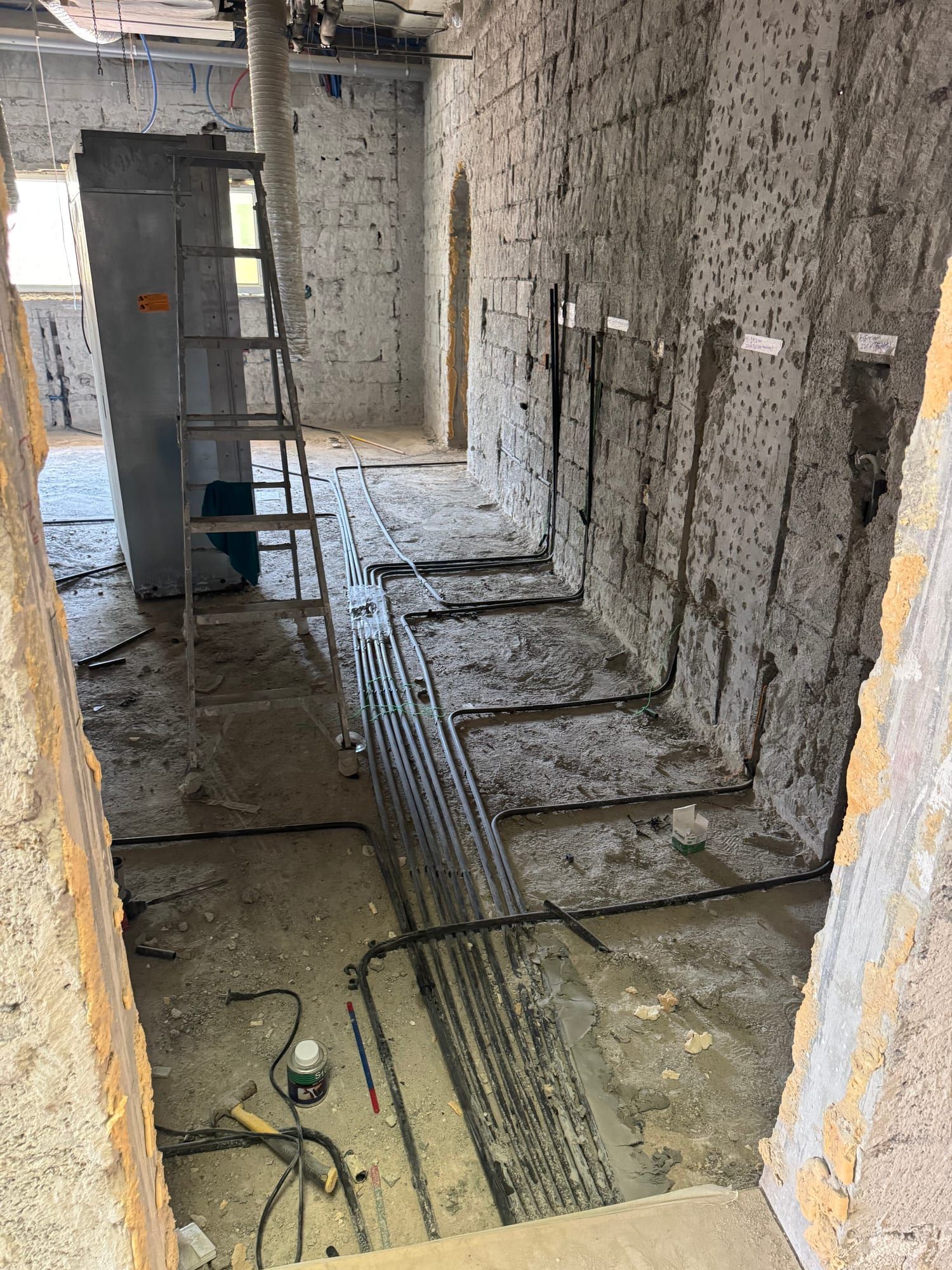 Corridor with conduit and pipe runs laid across the floor and chased into the stripped walls