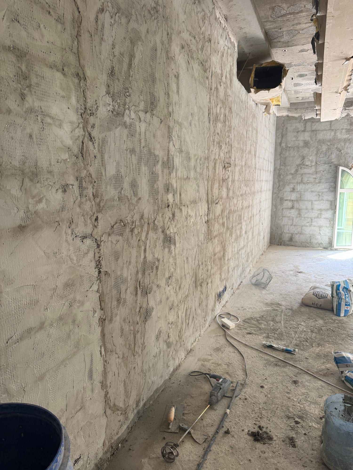 Long wall stripped of its surface, showing blockwork and patches of old render along its length