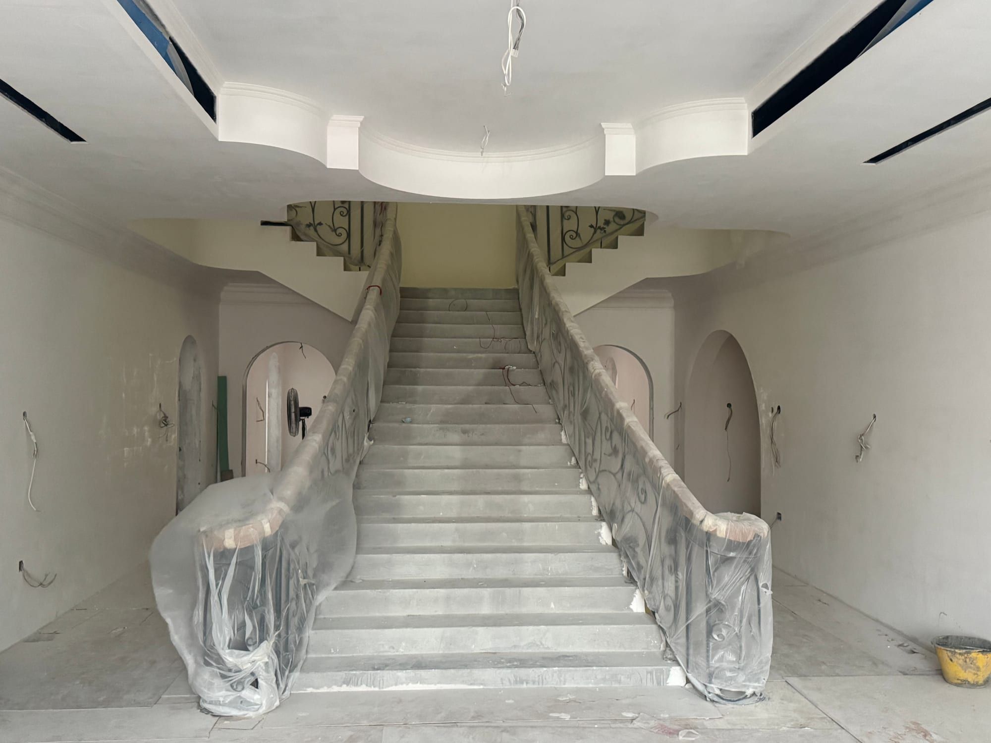 Double staircase under protective wrap in the entrance hall, with the stepped ceiling above