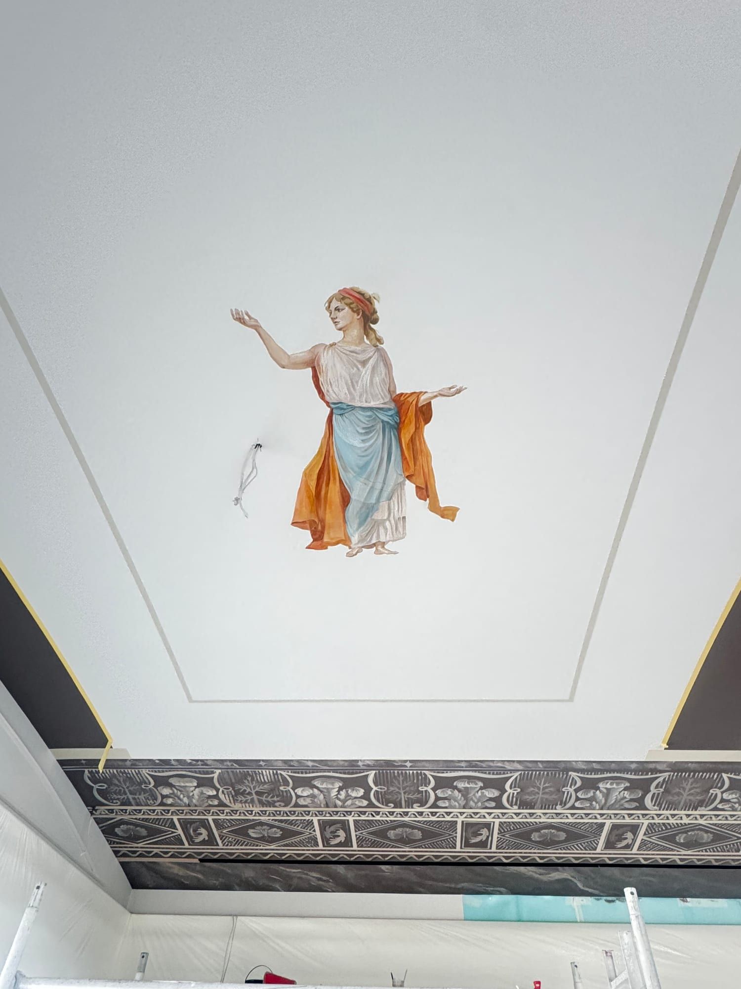 Painted figure of a woman in a blue and orange robe on a white ceiling panel
