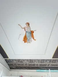 Painted figure of a woman in a blue and orange robe on a white ceiling panel