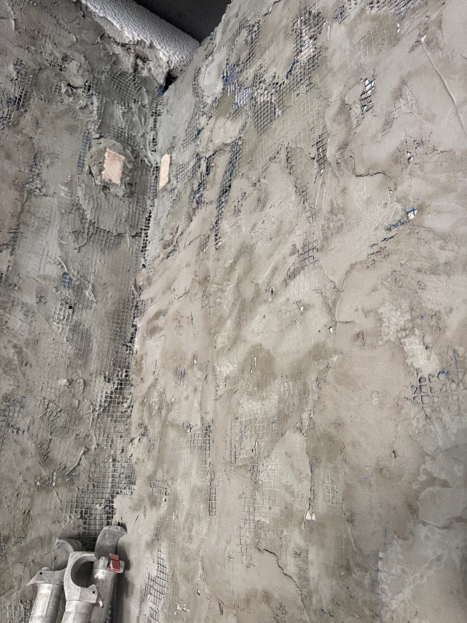 Corner of a wall where fresh plaster is being applied over reinforcing mesh