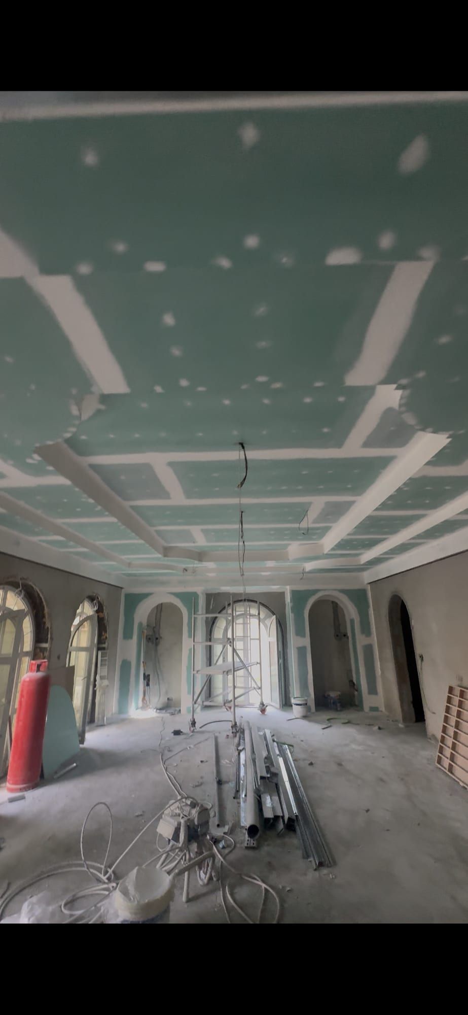 Stepped ceiling built in green board with its joints filled, above a room with arched windows